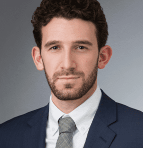 Zack Goldberg short brown hair, wearing a blue blazer, white shirt and gray tie